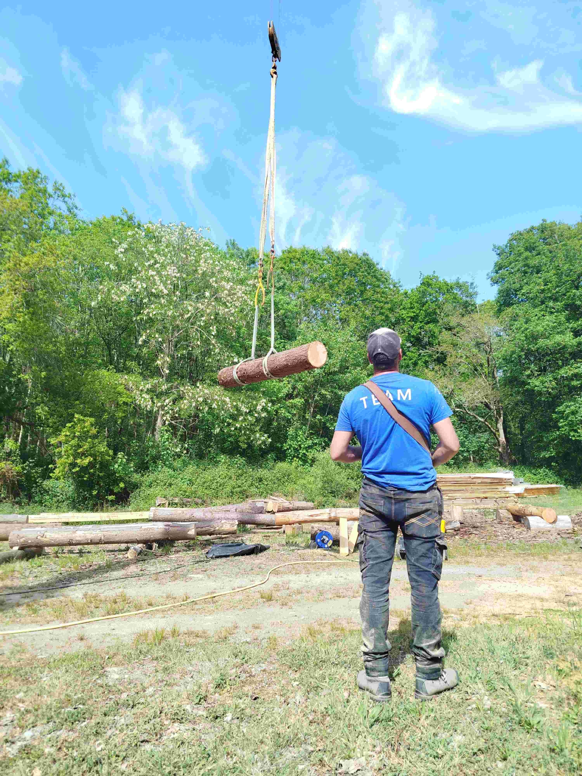 stagiaire à la commande de la grue pour déplacer un rondin de pin douglas bois brut à l'atelier TST, fustier constructeur de maisons en rondins près de Nantes