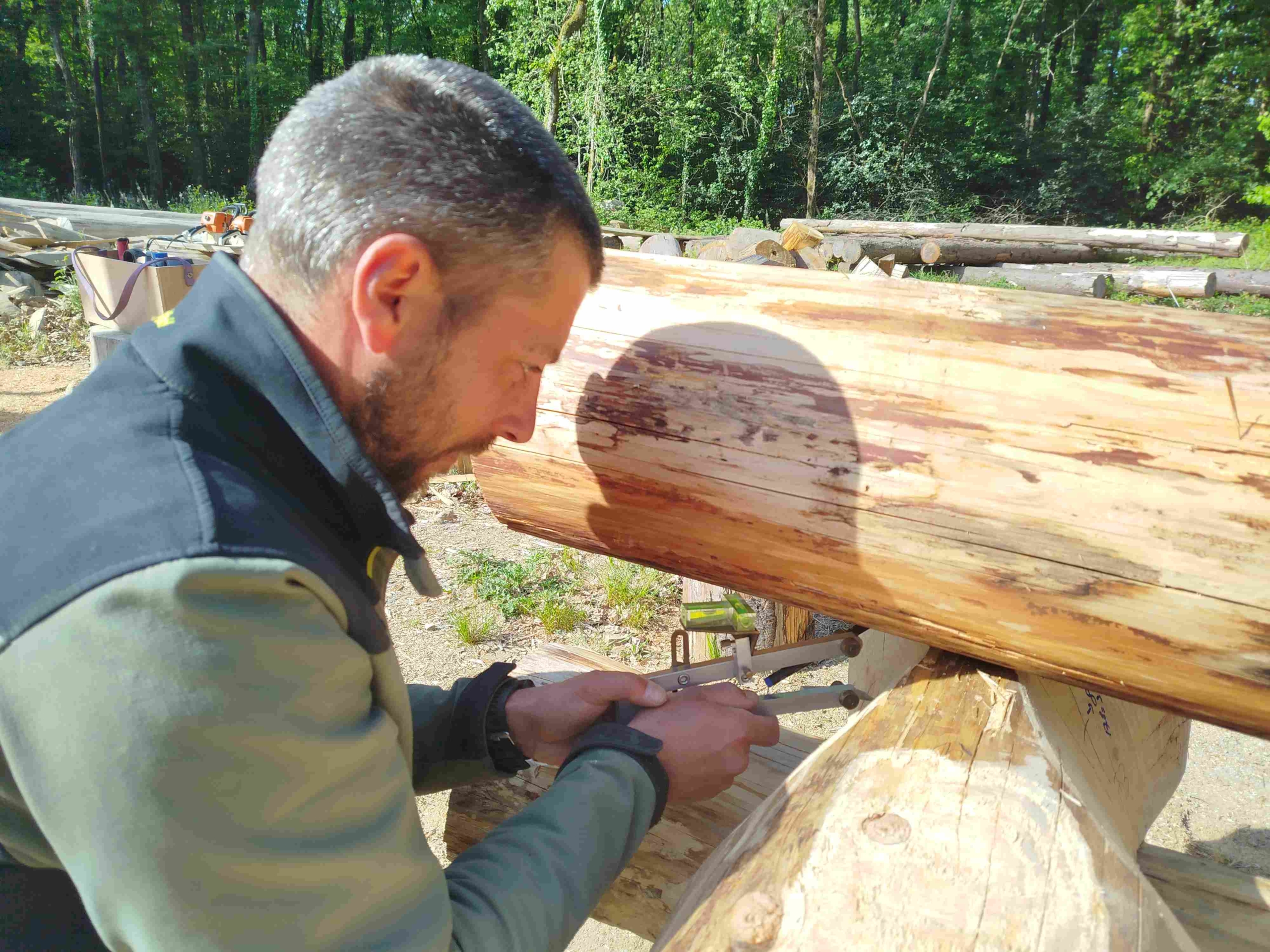 stagiaire qui trace au compas sur du pin douglas à l'atelier TST, fustier constructeur de maisons en rondins près de Nantes