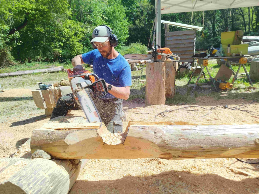 stagiaire qui découpe des rondins de pin douglas à l'atelier TST, fustier constructeur de maisons en rondins près de Nantes
