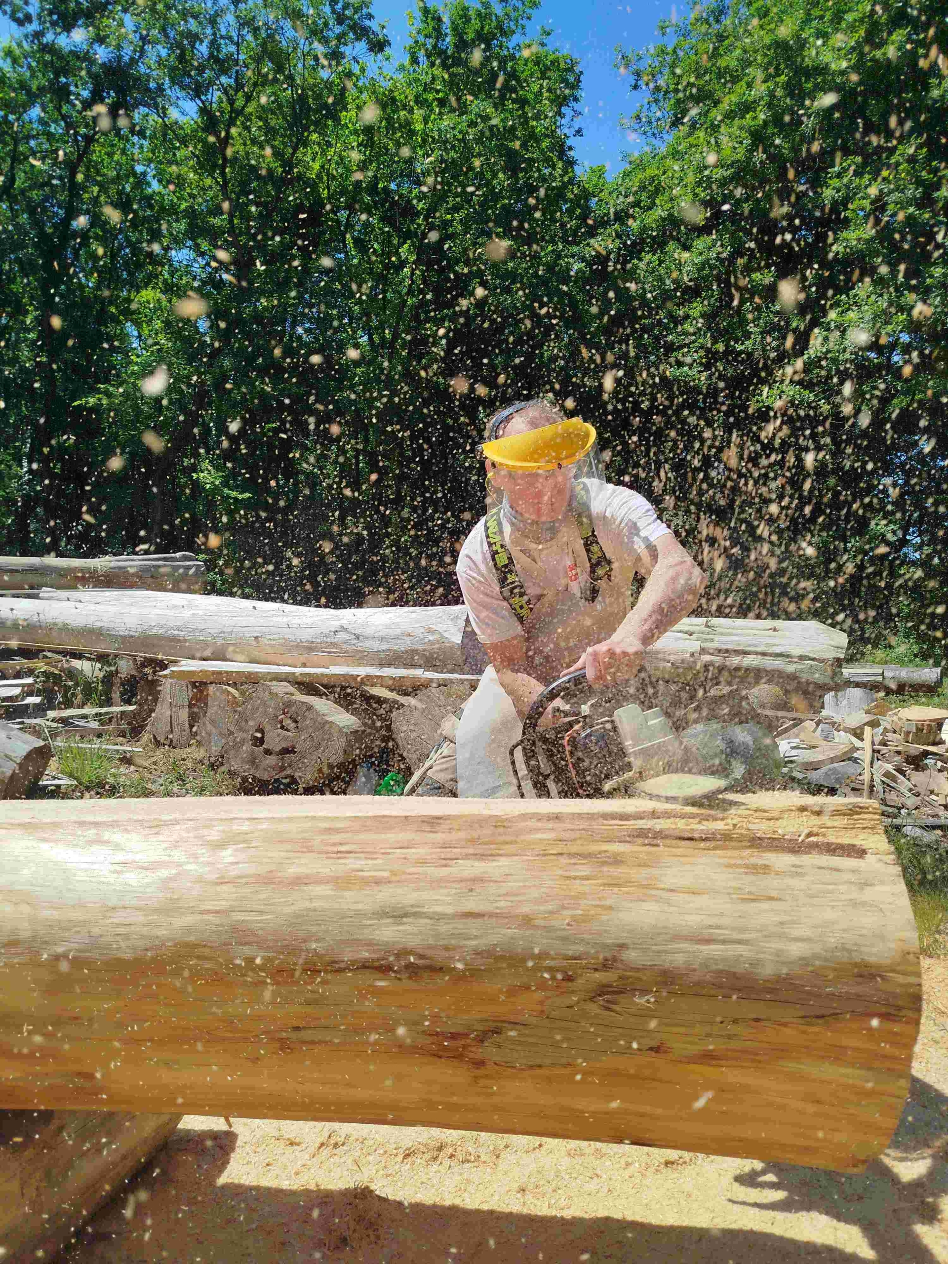 Artisan fustier constructeur de maison en rondins taillant un rondin à la tronçonneuse, atelier TST près de Nantes